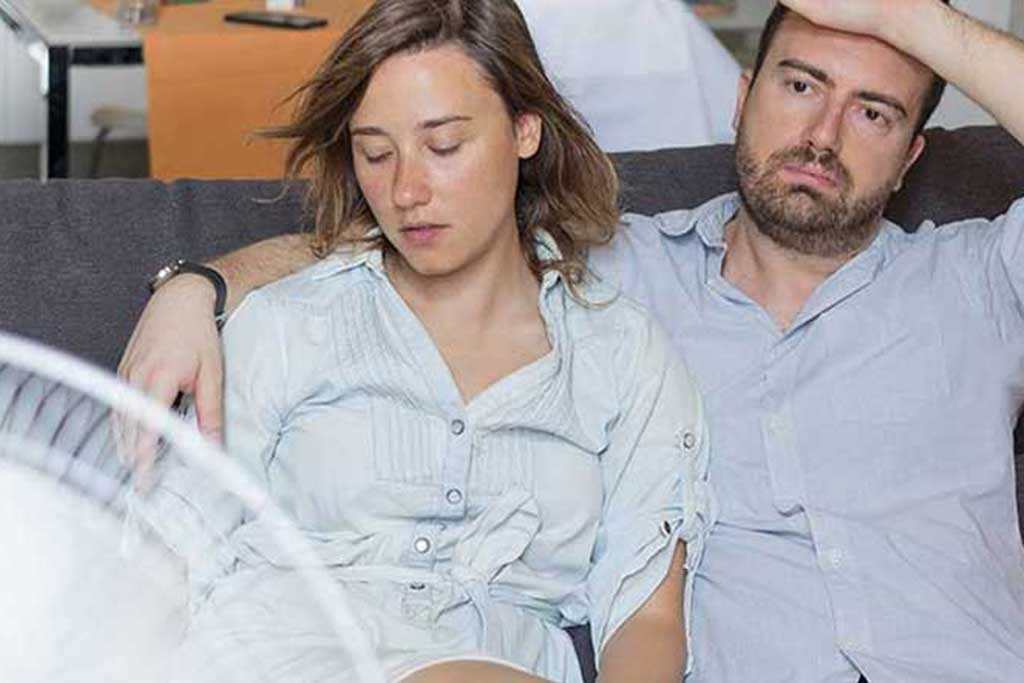 Couple sitting in front of a fan in a hot house